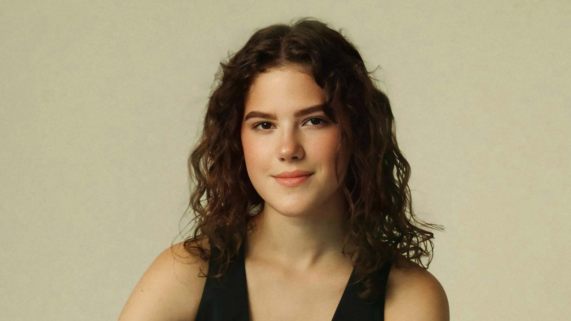 A portrait of a young adult woman with curly brown hair and a black tank top