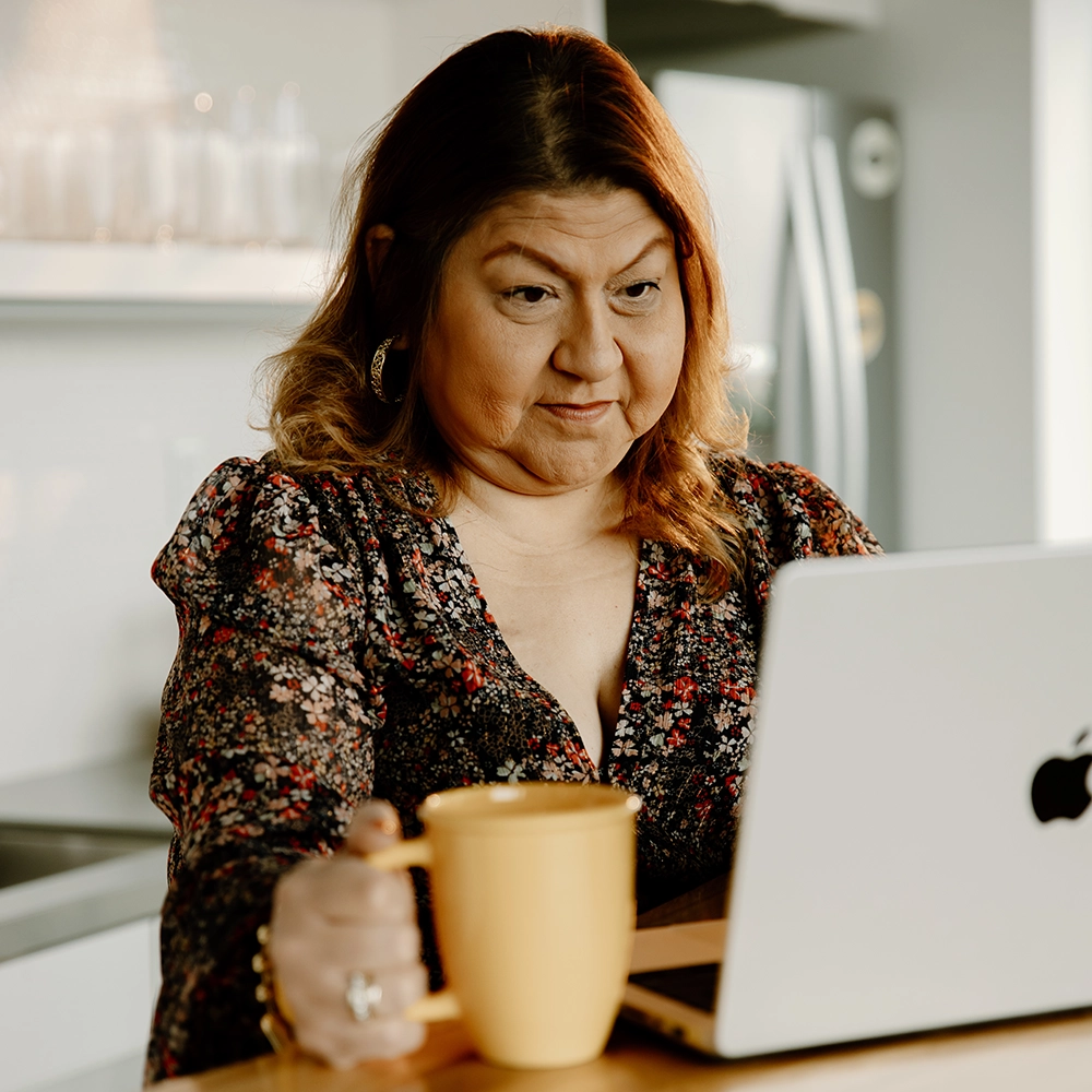 A woman using a laptop while holding a yellow mug